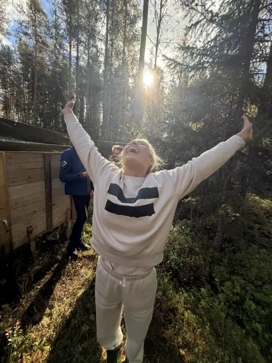 Anja strekker armene mot sola i skogen, ute av kassen.